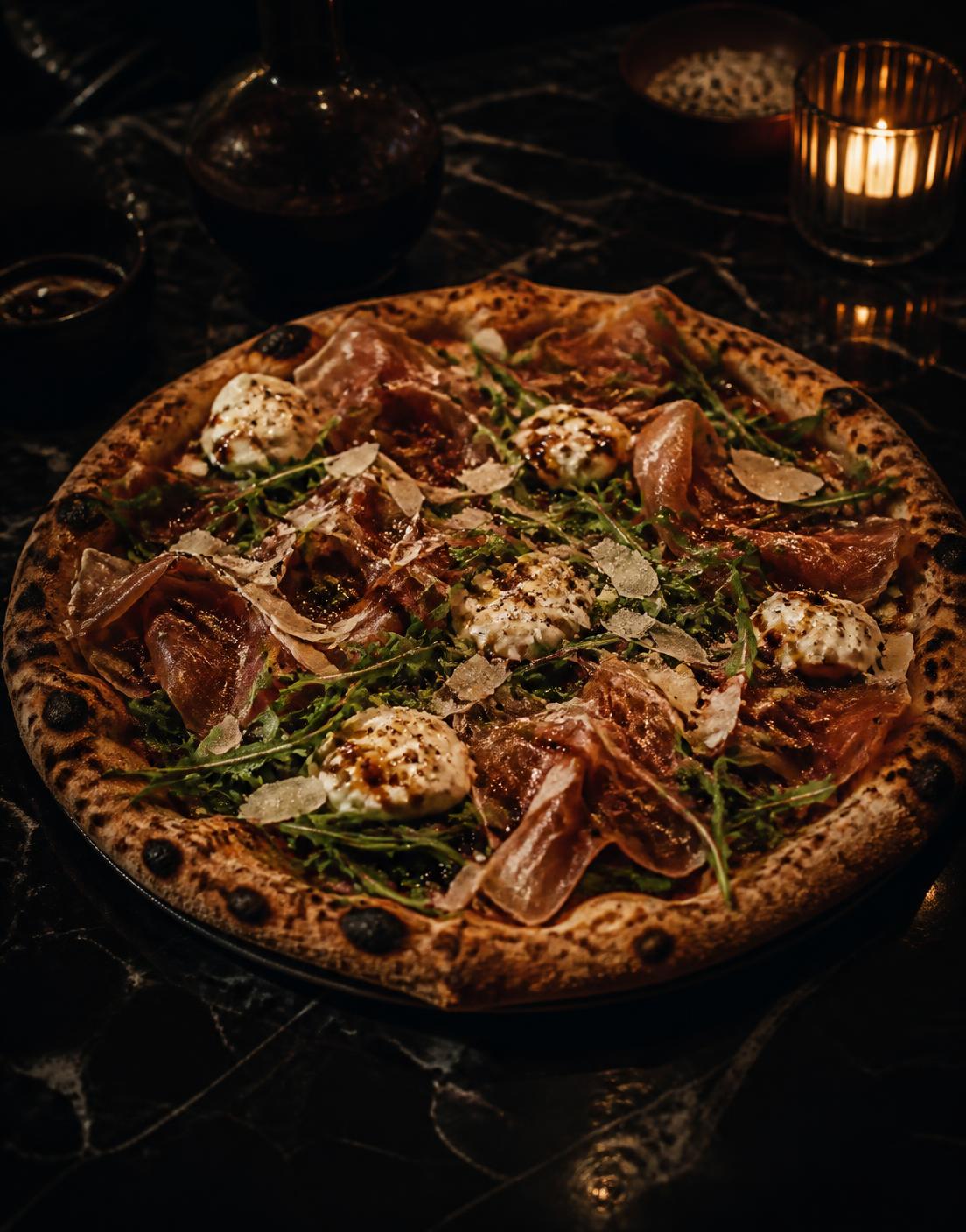 Pizza crowned with draped Prosciutto di Parma, stracciatella and wild arugula on black marble